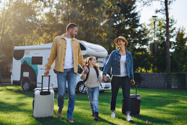 A happy young family walking with suitcases, coming home from caravan trip outdoors in garden