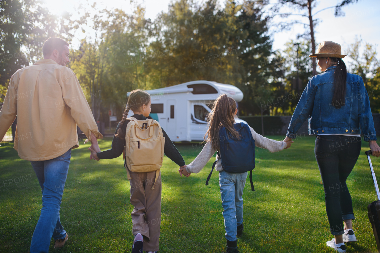 A rear view of young family with suitcases going to caravan outdoors at park.