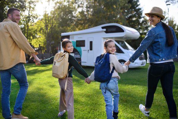 A rear view of young family with suitcases going to caravan outdoors at park.