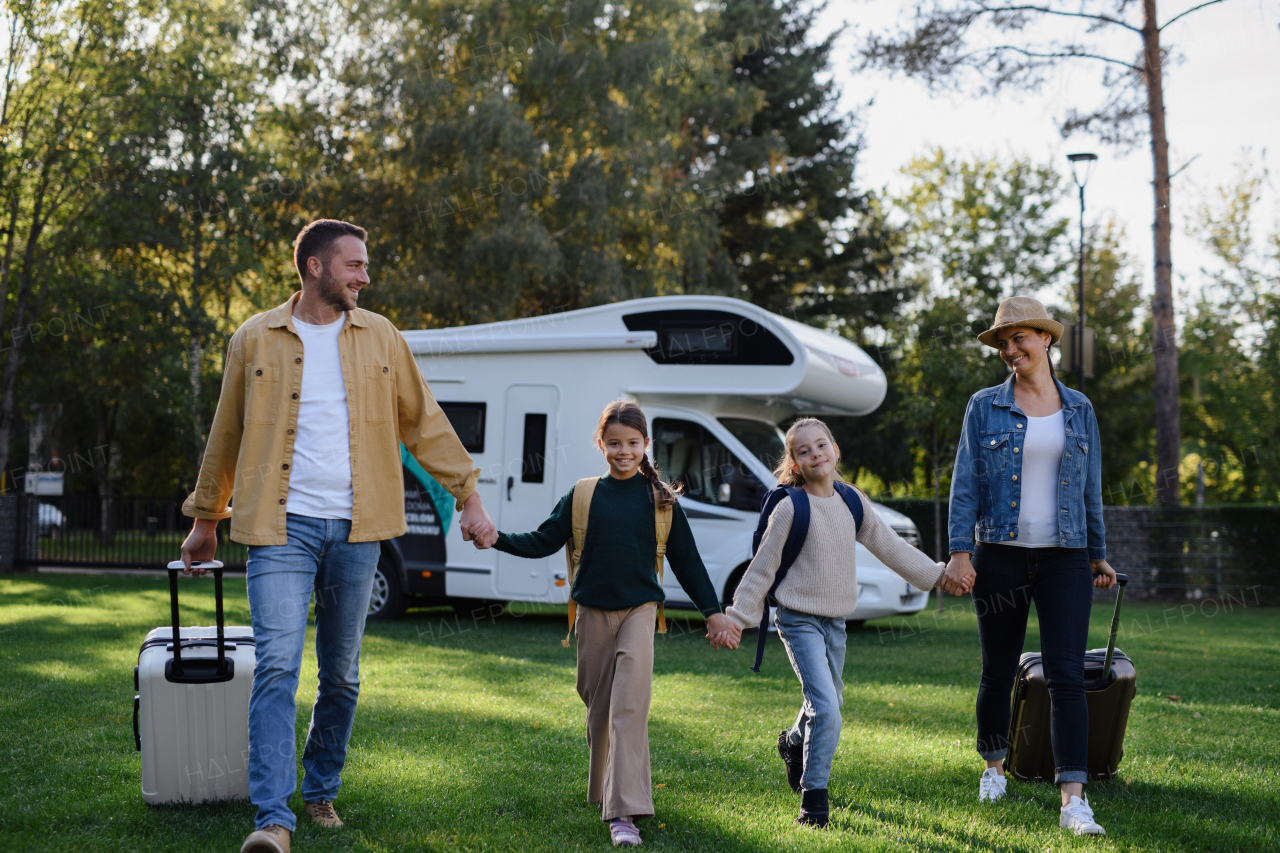 A happy young family walking with suitcases, coming home from caravan trip outdoors in garden