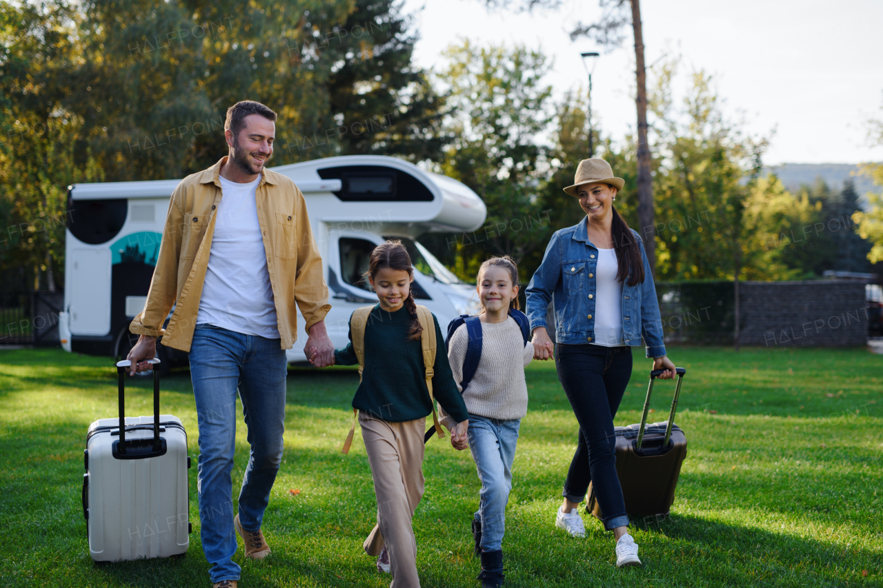 A happy young family walking with suitcases, coming home from caravan trip outdoors in garden