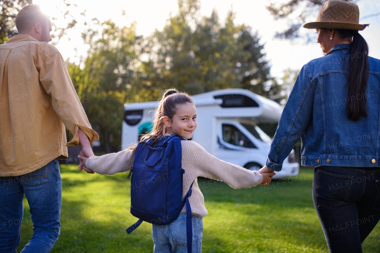 Rear view of a little girl looking at camera and holding parents when going to caravan outdoors at park.