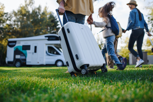 A rear view of young family with suitcases going to caravan outdoors at park.