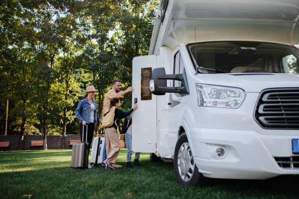 A young family with suitcases entering caravan outdoors at park.