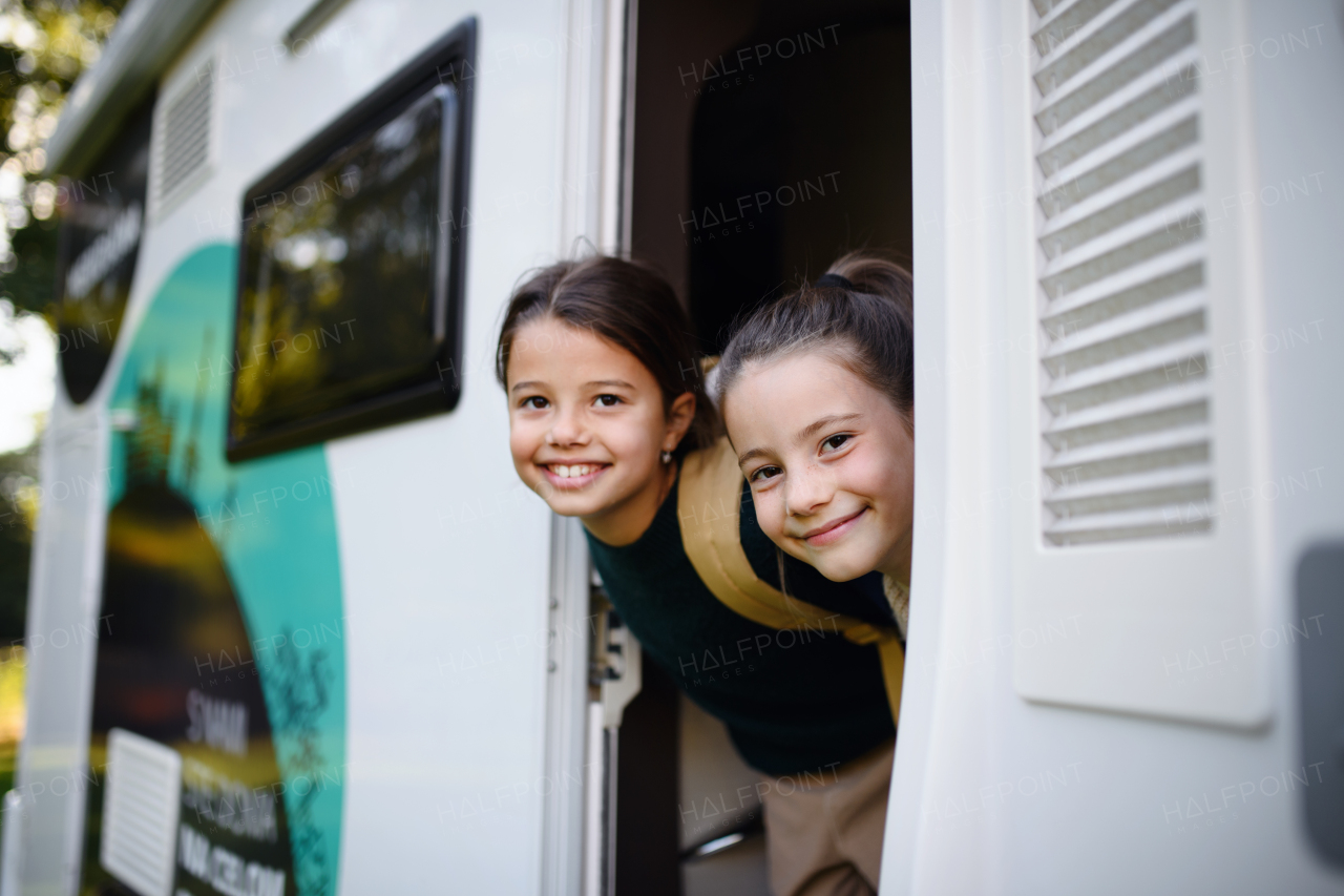 Happy two little girls looking out of caravan and smiling to the camera.