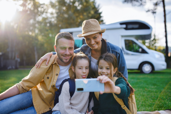 A happy young family with two children ltaking selfie with caravan at background outdoors.