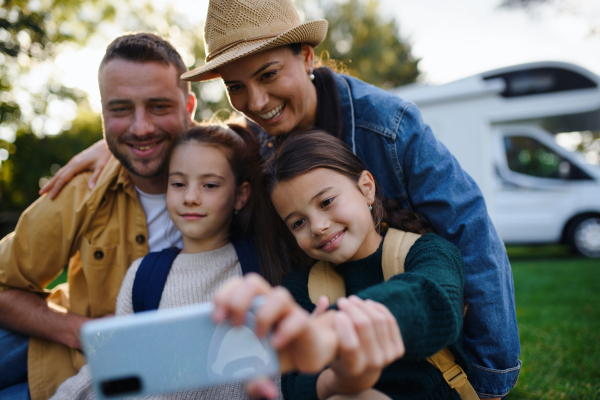 A happy young family with two children ltaking selfie with caravan at background outdoors.