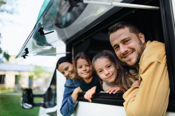 A happy young family with two children looking out of caravan window.