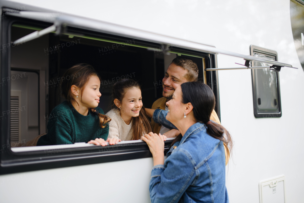 Happy two little girls with father looking out of a caravan window and talking to mother.