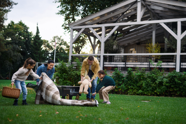 A happy young family with basket and blanket going to have picnic outdoors in restaurant area.