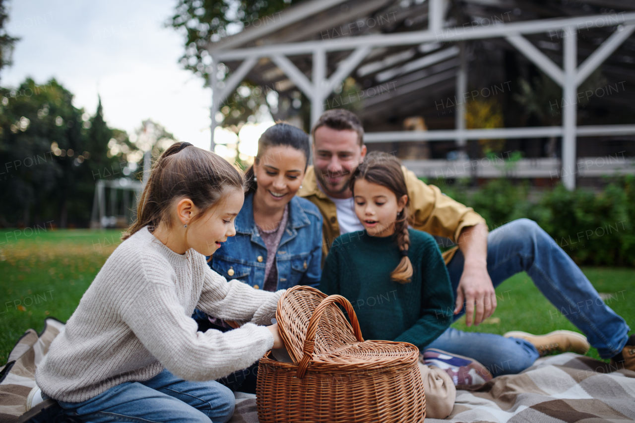 A happy young family sitting on blanket and having take away picnic outdoors in restaurant area.