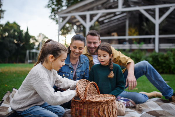 A happy young family sitting on blanket and having take away picnic outdoors in restaurant area.