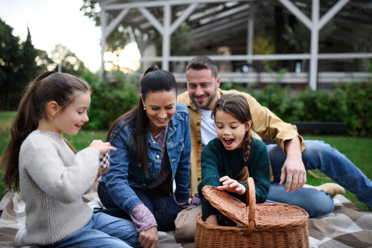 A happy young family sitting on blanket and having take away picnic outdoors in restaurant area.