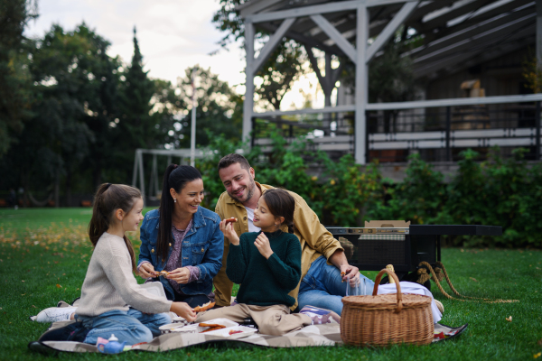 A happy young family sitting on blanket and having take away picnic outdoors in restaurant area.