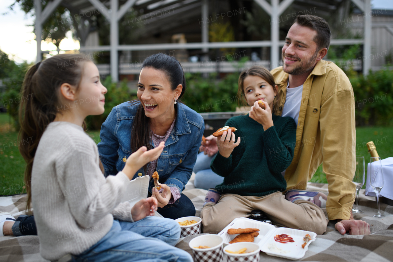 A happy young family sitting on blanket and having take away picnic outdoors in restaurant area.