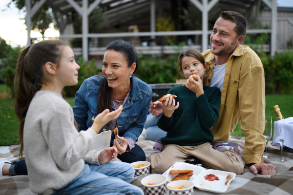 A happy young family sitting on blanket and having take away picnic outdoors in restaurant area.