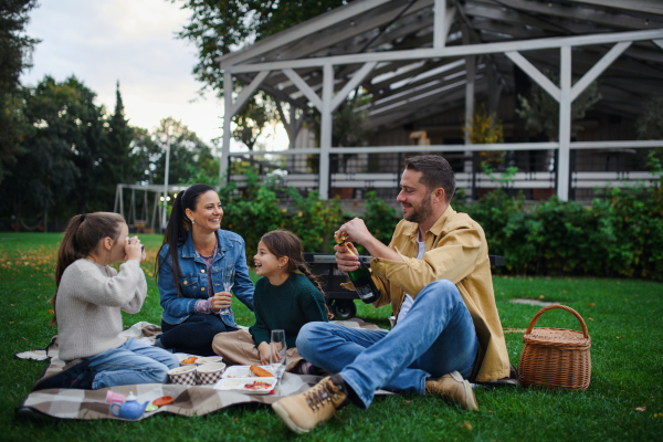 A happy young family sitting on blanket and having take away picnic outdoors in restaurant area.