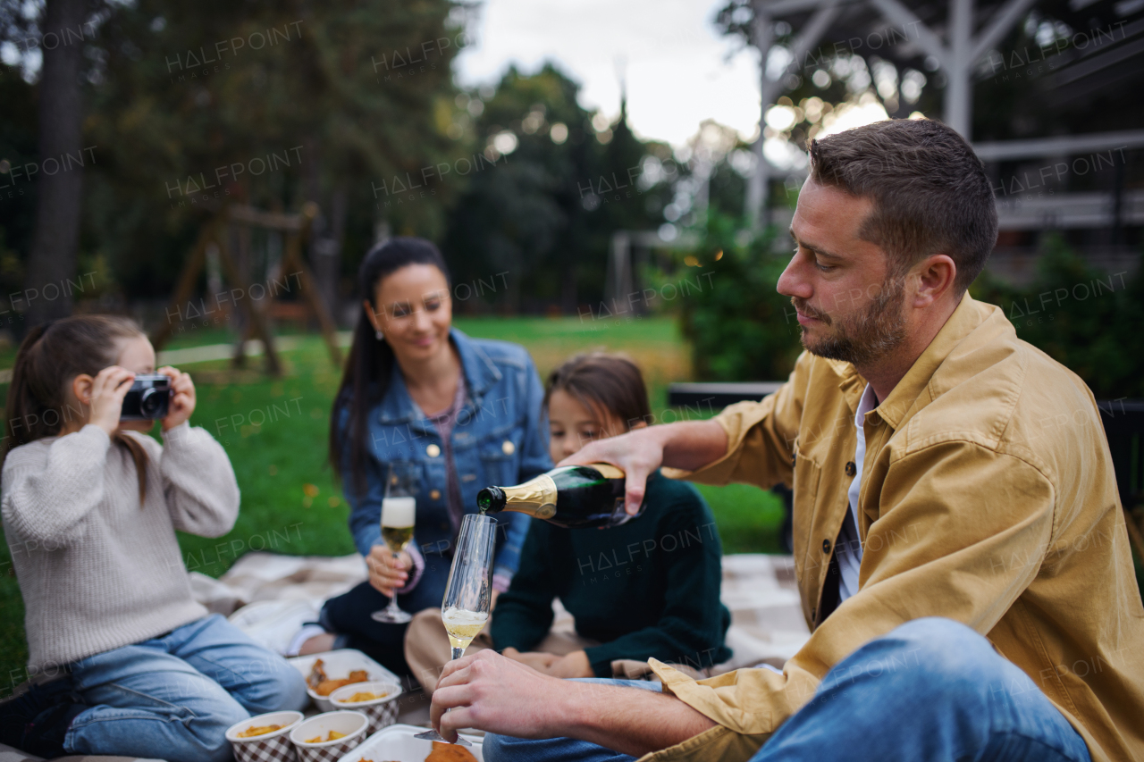 A happy young family sitting on blanket and having take away picnic outdoors in restaurant area.