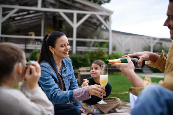 A happy young family sitting on blanket and having take away picnic outdoors in restaurant area.