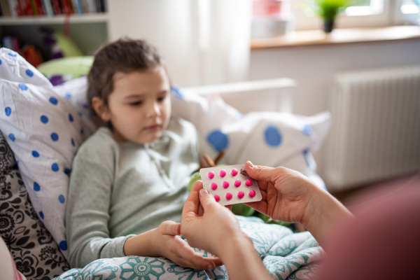 Portrait of mother looking after sick small daughter in bed at home, giving medicine.