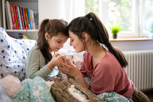 Portrait of mother looking after sick small daughter in bed at home.