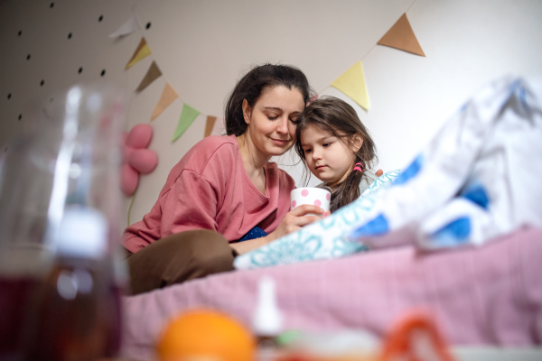 Portrait of mother looking after sick small daughter in bed at home.