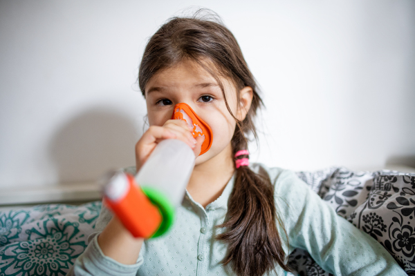 A portrait of sick small girl at home, using inhaler.