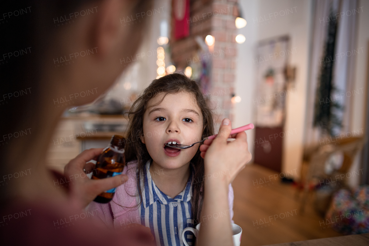 Portrait of mother looking after sick small daughter at home, giving syrup.