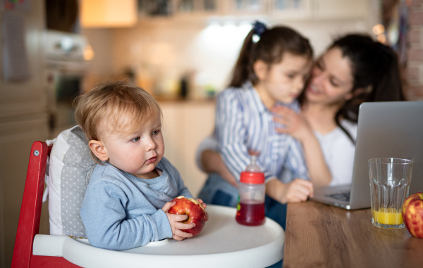 Portrait of small toddler girl with mother and sister, sitting in highchair.