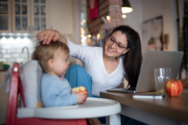 Happy mother with small daughter in kitchen, home office with children concept.