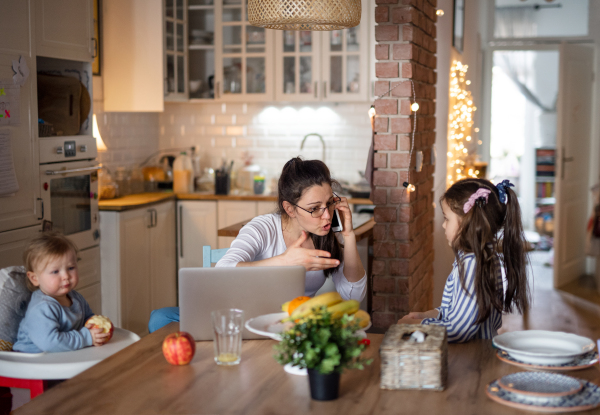 Angry mother with two small daughters in kitchen, home office concept.