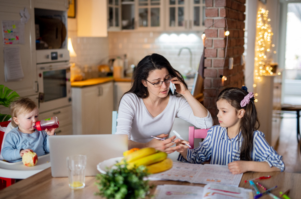 Portrait of mother with small daughter in kitchen, home schooling, office and distance learning concept.