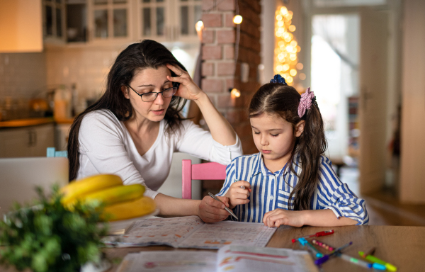 Portrait of mother with small daughter in kitchen, home schooling and distance learning concept.