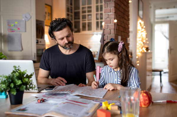 Mature father with small daughter in kitchen, distance learning, home office and schooling concept.