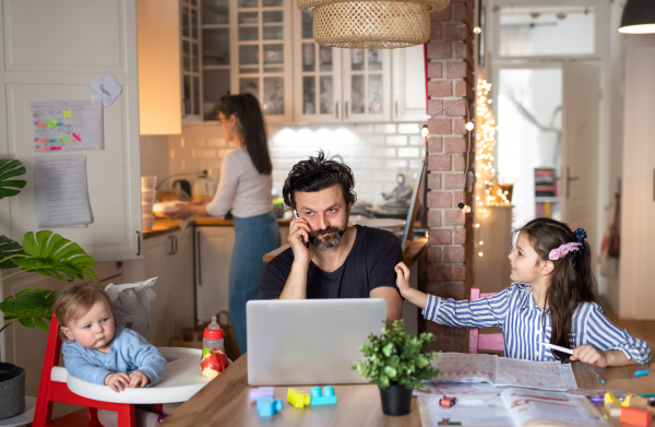 Mature father with small daughters in kitchen, distance learning, home office and schooling concept.