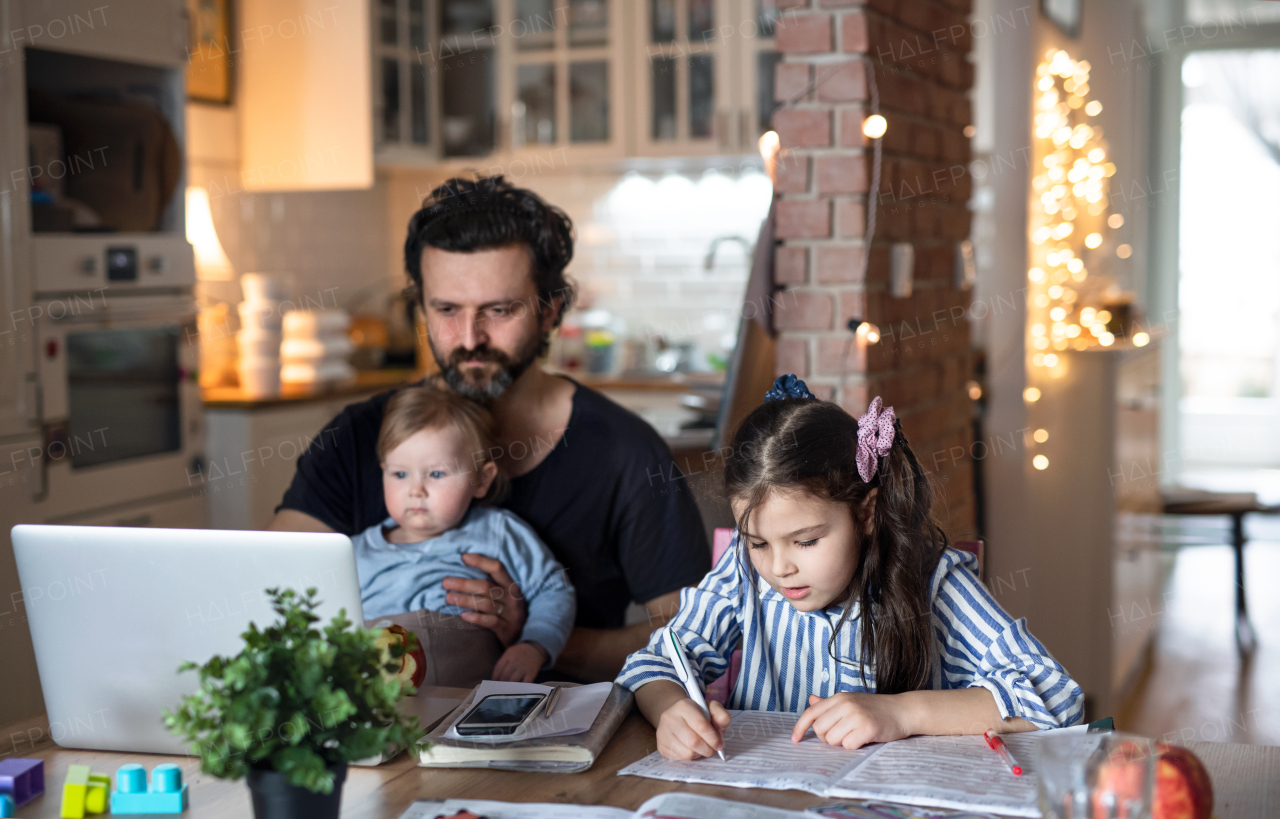 Mature father with small daughters in kitchen, distance learning, home office and schooling concept.