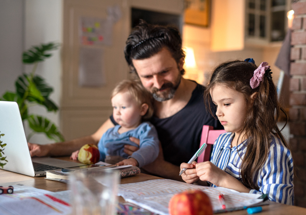 Mature father with small daughters in kitchen, distance learning, home office and schooling concept.