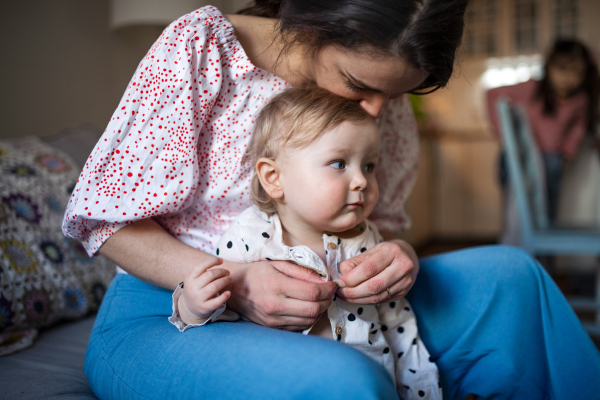 Happy mother with small toddler daughter in bedroom at home, getting dressed.