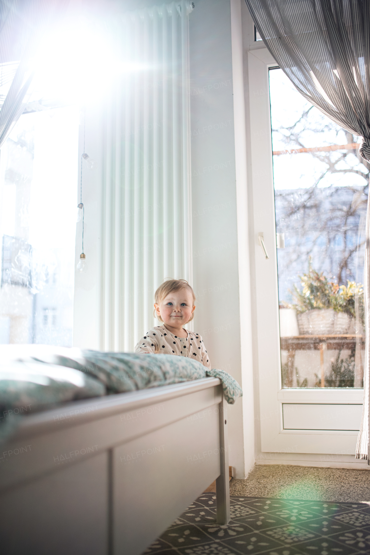 Happy small toddler girl walking by bed in bedroom at home, first steps concept.