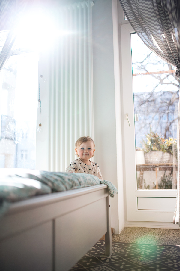 Happy small toddler girl walking by bed in bedroom at home, first steps concept.