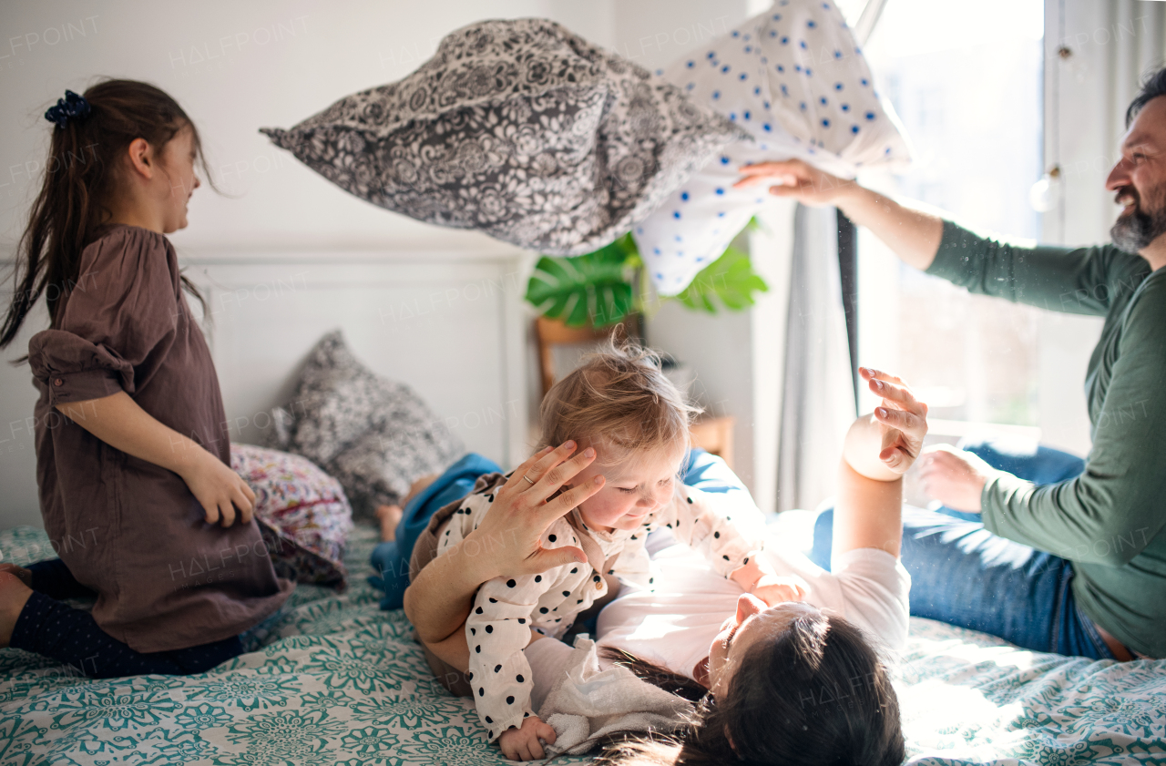 Portrait of happy family with two small daughters having fun on bed at home.