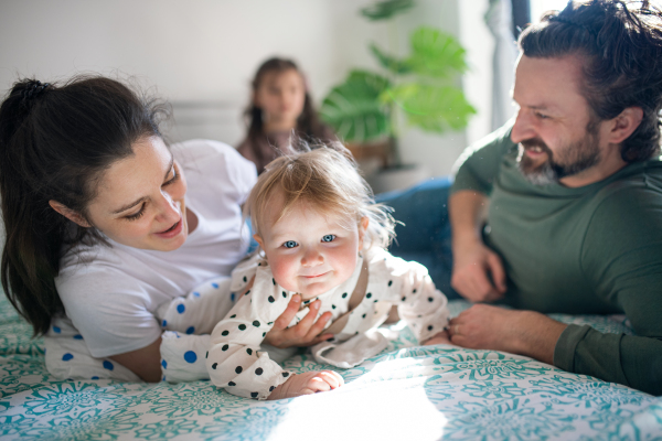 Portrait of happy family with two small daughters having fun on bed at home.