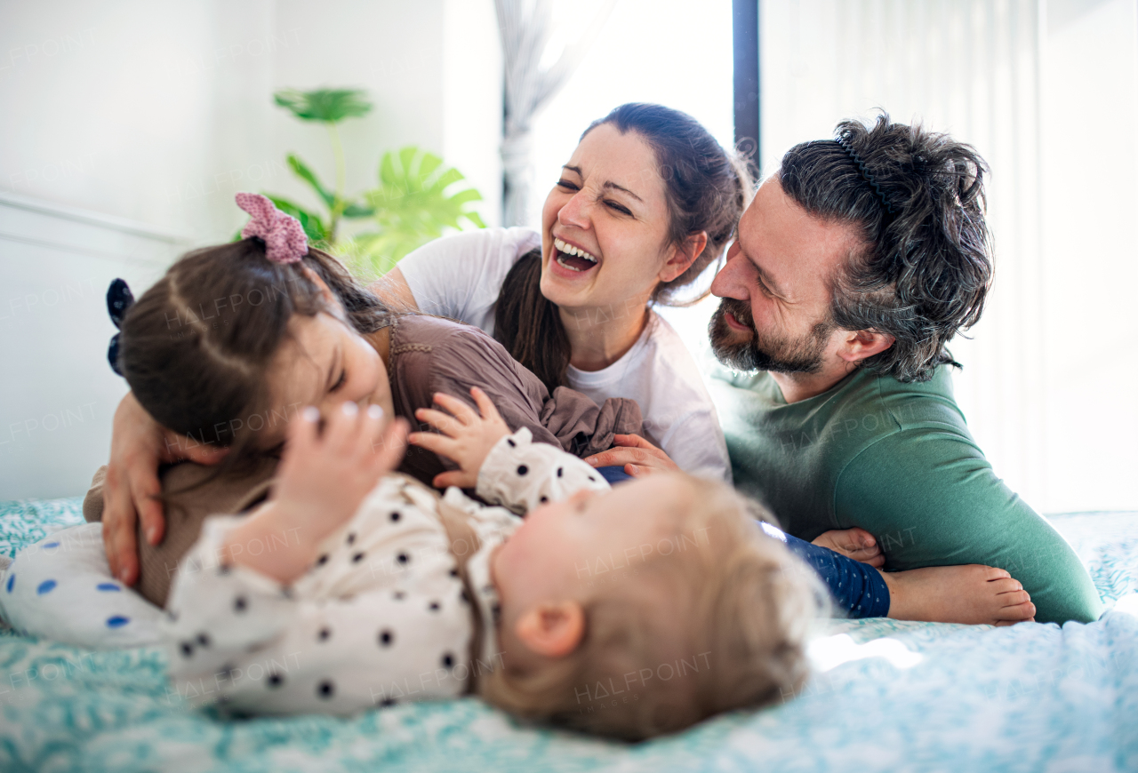 Portrait of happy family with two small daughters having fun on bed at home.