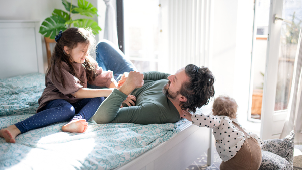 Portrait of happy father with two small daughters having fun on bed at home.