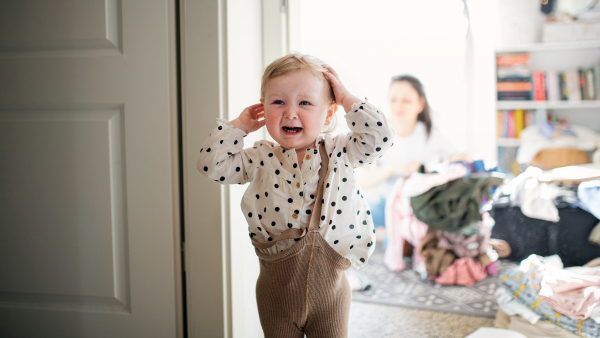 An upset small toddler girl in bedroom at home, crying.