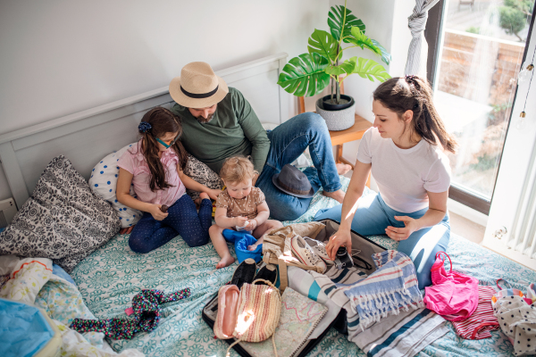 A top view of family with two small daughters packing for holiday on bed at home.