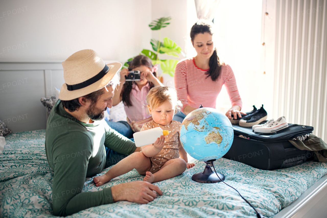 Portrait of family with two small daughters packing for holiday on bed at home.