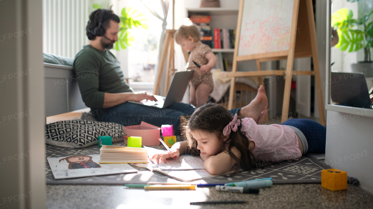 Busy father working with small daughters in bedroom, home office concept.