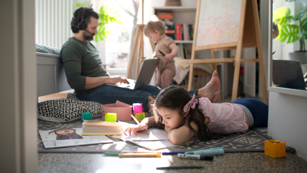 Busy father working with small daughters in bedroom, home office concept.