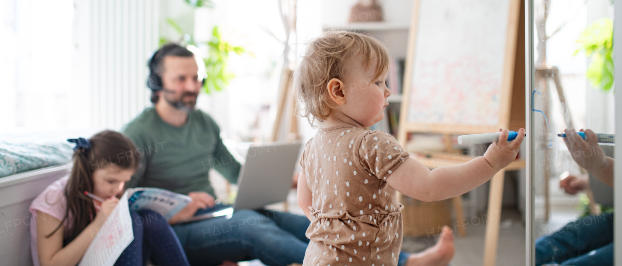 Busy father working with small daughters in bedroom, home office concept.